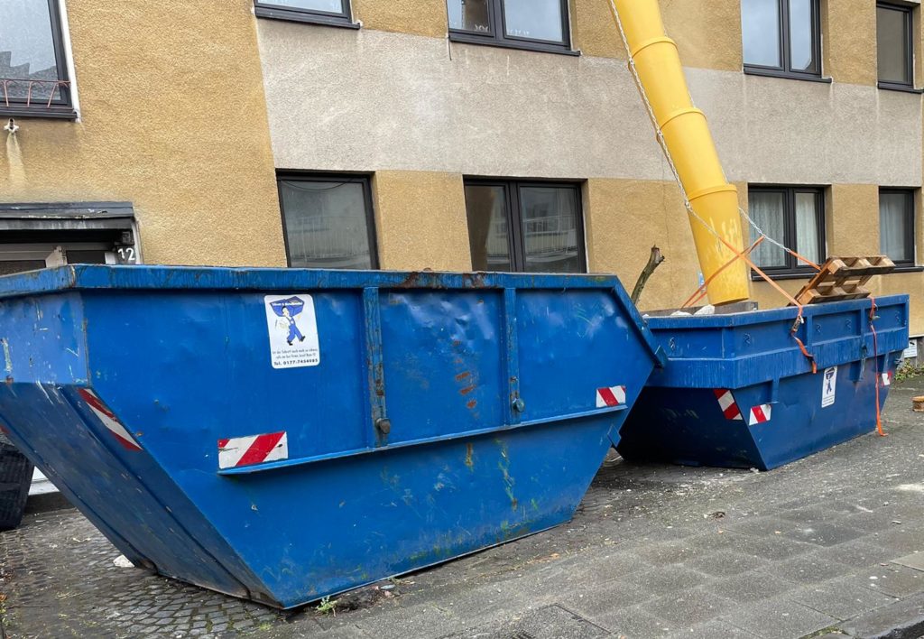 Zwei Müllcontainer stehen da, in die Abfall durch einen Baustellen-Müllschacht geworfen wird